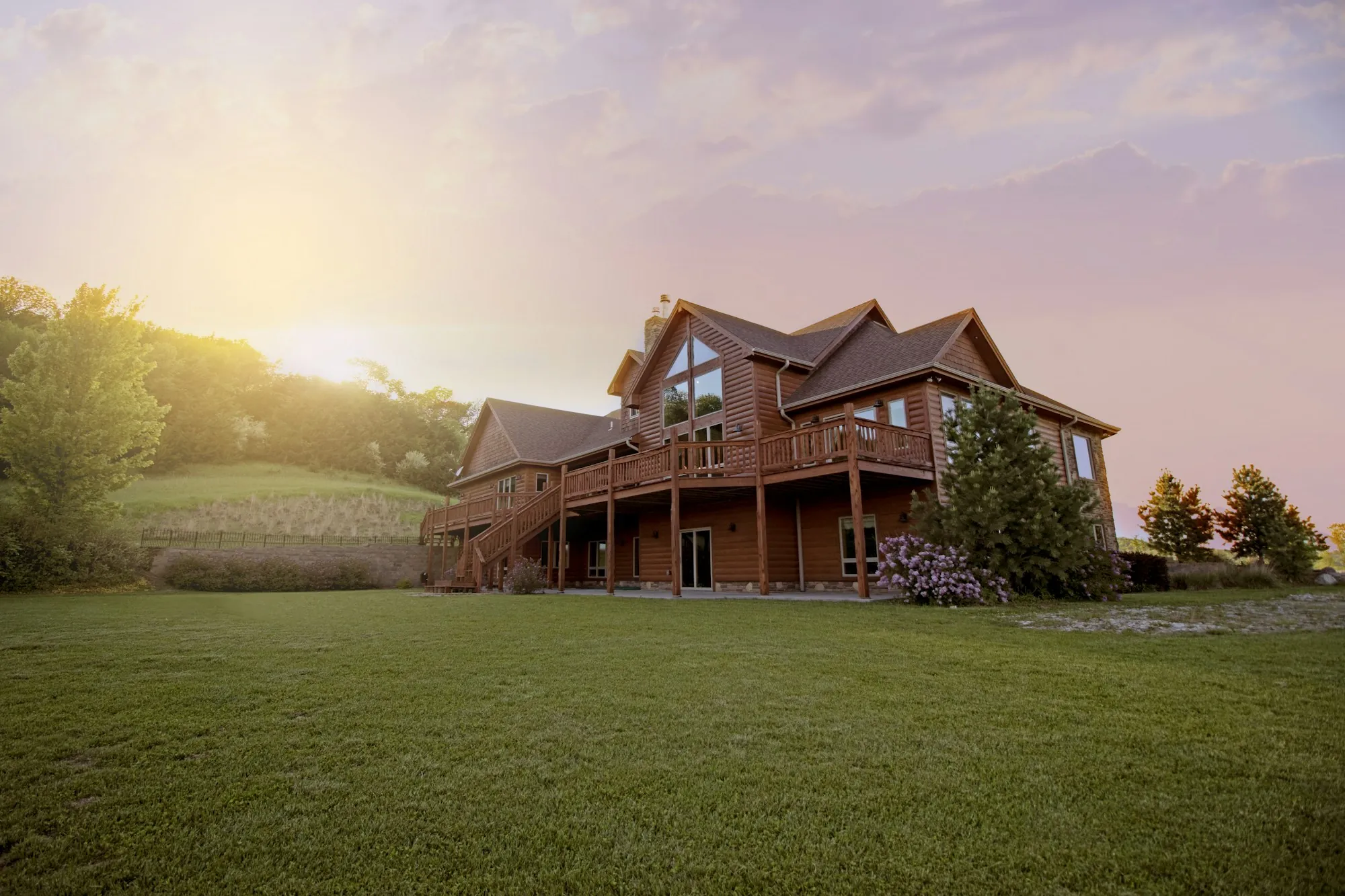 Wood-sided two-story house above a sloping lawn at sunset